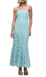 A woman wears the Clairis Lace Bustier Midi Dress by Simkhai—featuring a strapless guipure lace design with intricate patterns and a bustier bodice—paired with sandals, set against a white background.