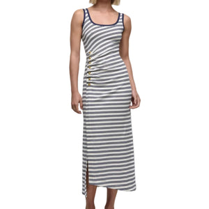 A woman wears the Simkhai Becker Cotton Jersey Midi Dress—sleeveless, white with navy stripes, side buttons, and a side slit—paired with white strappy sandals.