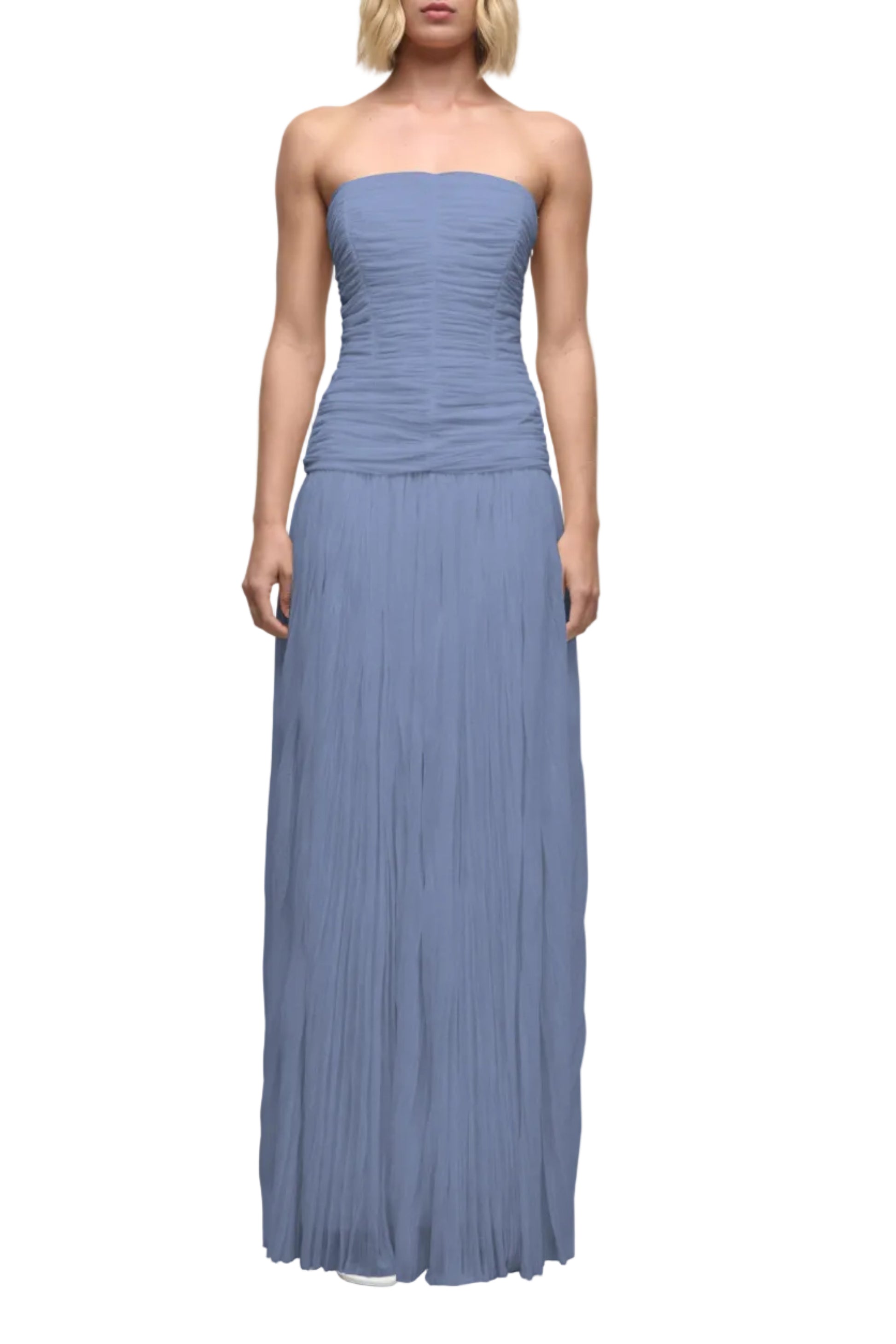 A woman stands against a white background wearing the Simkhai Danielle Crinkle Jersey Bustier Gown in light blue, featuring a strapless design with a ruched bodice and flowing sheer jersey skirt.