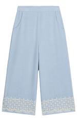 The Girls’ Florelia Pants by Louise Misha are light blue wide-leg Oxford cotton trousers with pockets, an elasticized waist, and delicate white embroidered lace detail along the hem.