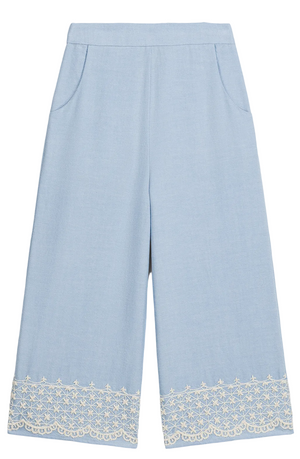 The Girls’ Florelia Pants by Louise Misha are light blue wide-leg Oxford cotton trousers with pockets, an elasticized waist, and delicate white embroidered lace detail along the hem.