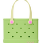 Light green Bitty Bogg® Bag by Bogg Bags, a compact tote featuring cream handles, round holes throughout, pink button accents, and a pink “bogg” logo at the bottom right corner. This washable bag is perfect for everyday use.