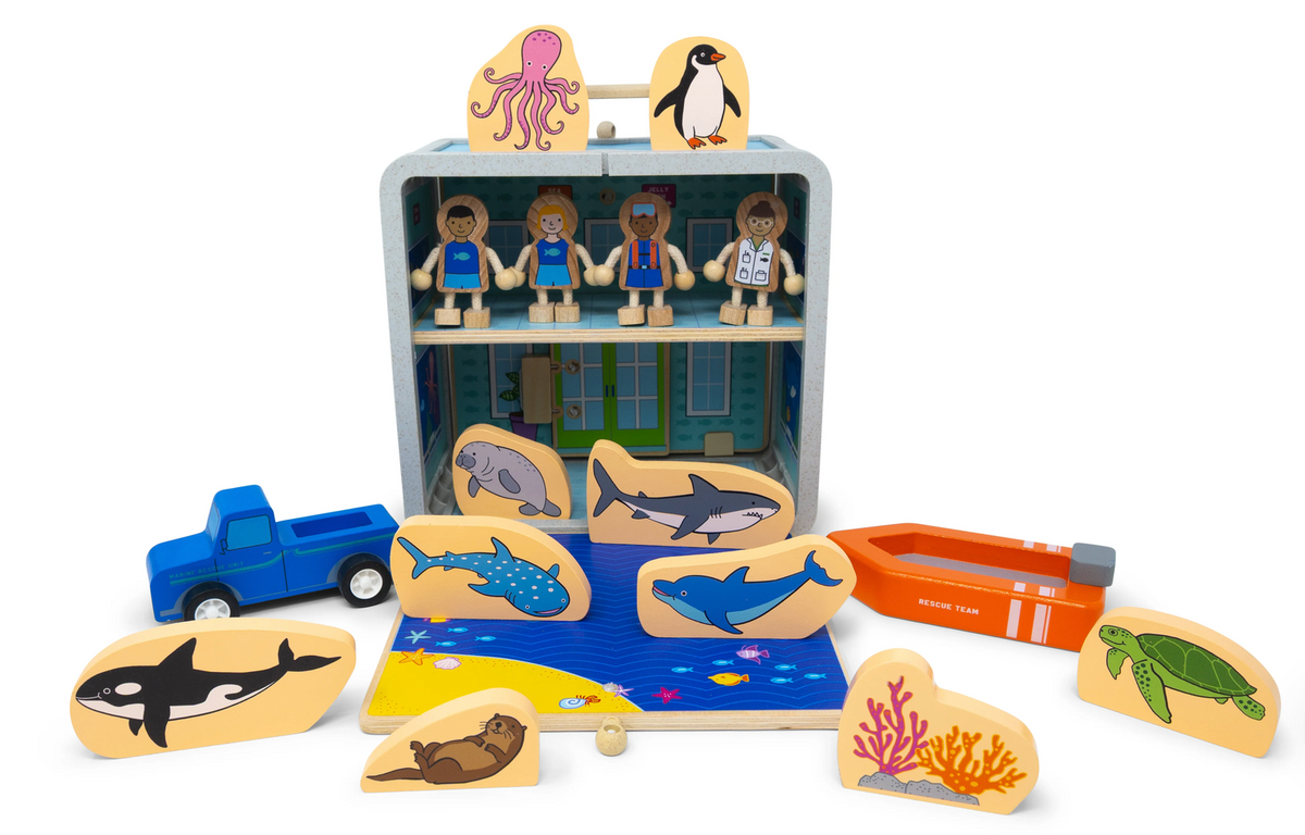 Jack Rabbit Creations Suitcase Series set featuring an open bamboo suitcase, wooden figures, marine animal cutouts, a blue truck, and an orange rescue boat with non-toxic paints.
