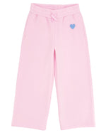 The Girls’ Cozy Sweatpant by Feather 4 Arrow features a light pink, wide-leg design with an elastic waistband, front pockets, flared bottoms, and a small blue heart detail on the left side.