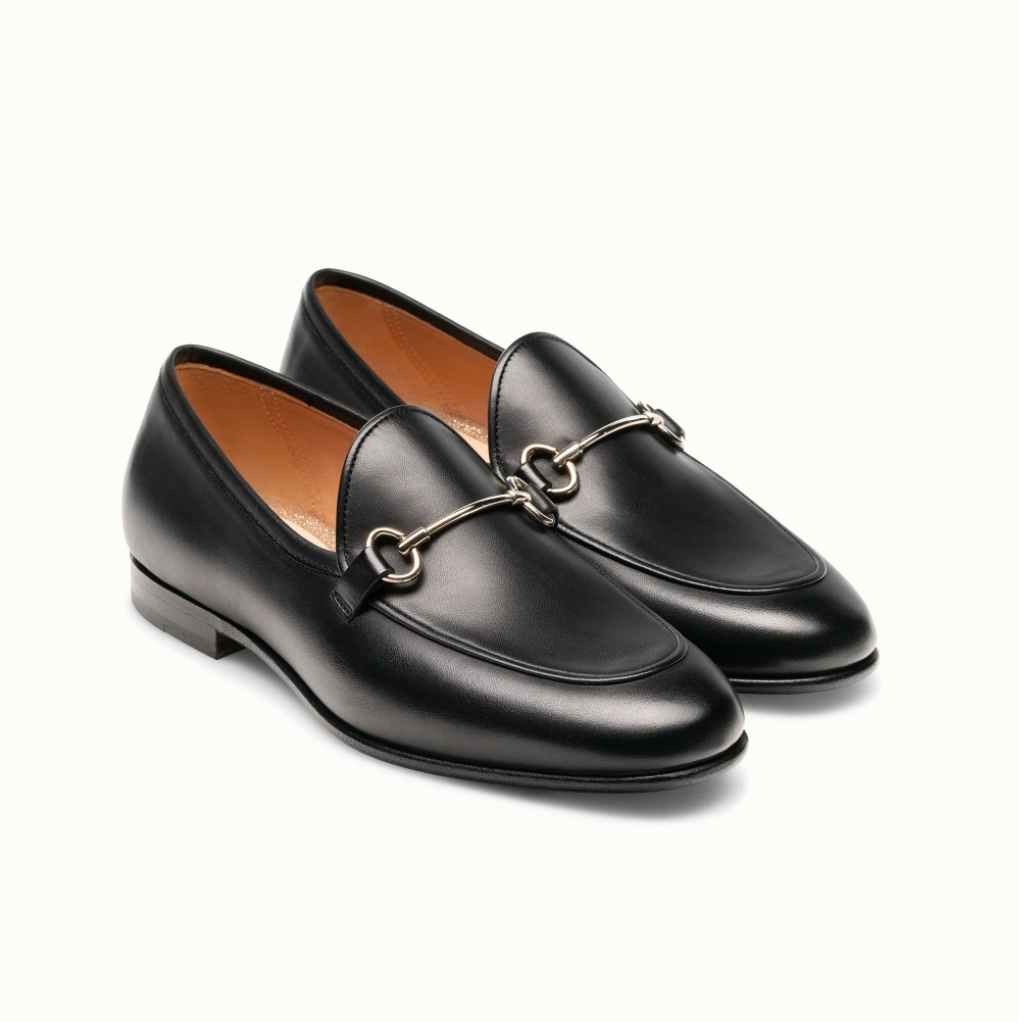 The Magnanni Stella Loafer, a pair of black leather apron toe loafers with metal bit detail, low heels, and tan lining, is shown side by side on a white background.