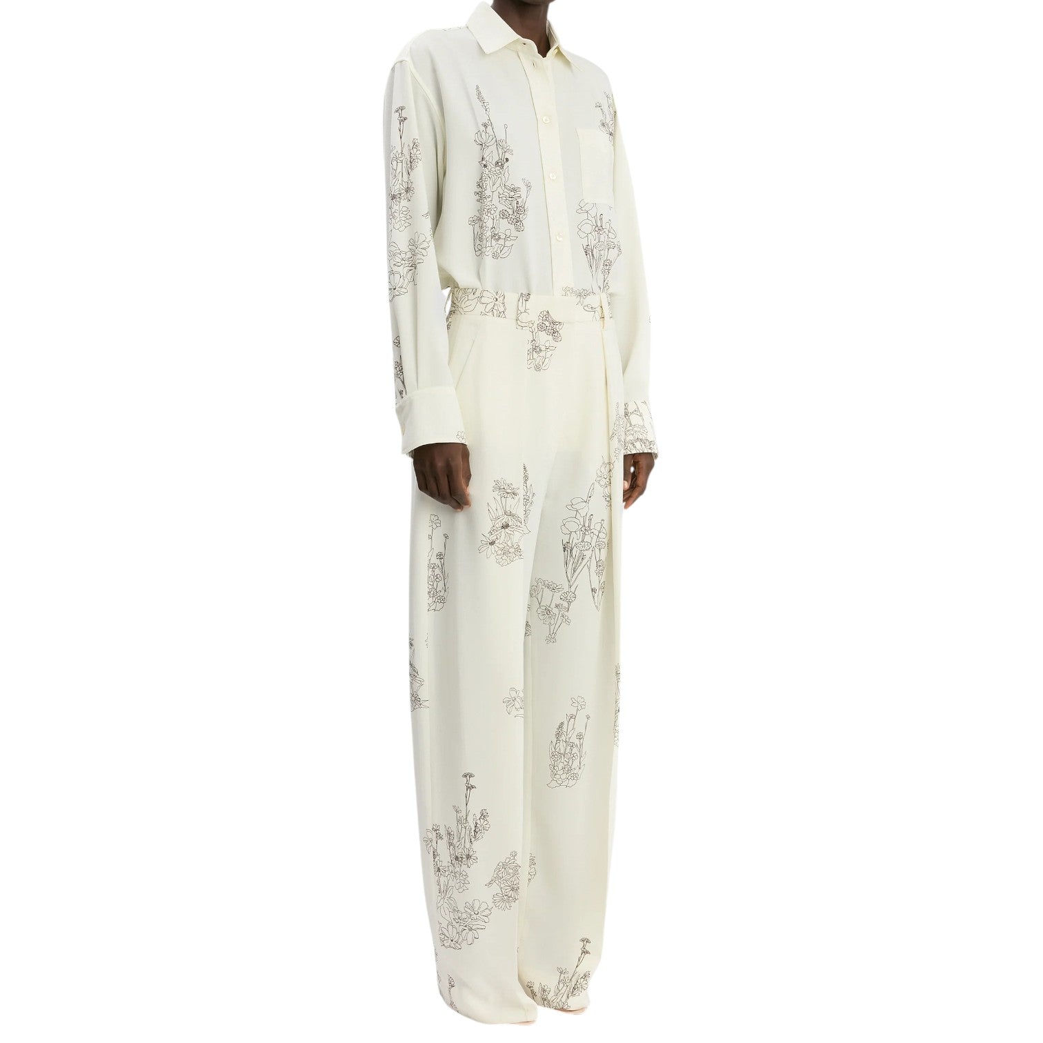 A person wearing Victoria Beckham’s Floral Wide Leg Trouser—a loose-fitting, high-rise black/off white style featuring all-over floral line art and wide leg silhouette.