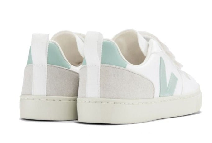 The Veja Kids' V-10 Velcro CWL Sneaker, made in Brazil, features a pair of white sneakers with light green accents and thick white soles, viewed from the back.