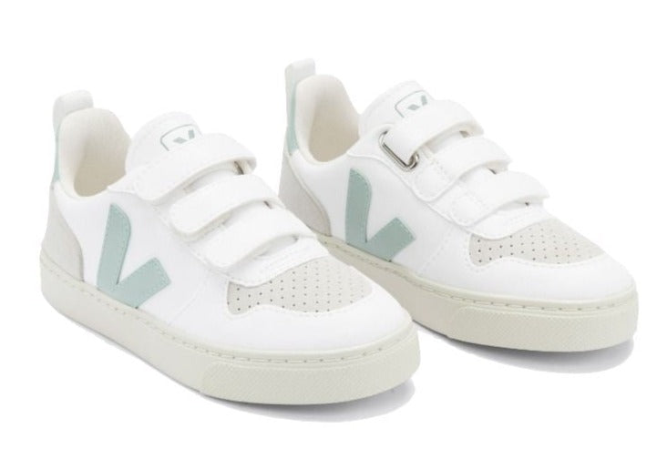 The Veja Kids' V-10 Velcro CWL Sneaker by Veja is a stylish pair of white sneakers with light grey and green accents. They feature two velcro straps, perforated detailing on the toe area, and are crafted from organic cotton and Amazonian rubber.