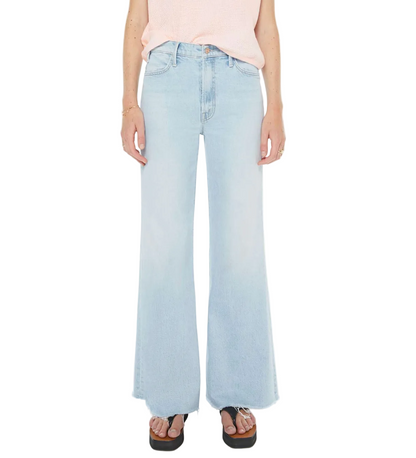 A person wearing The Hustler Roller Skimp Fray high-rise light blue wide-leg jeans by Mother, paired with a sleeveless light pink top, platform sandals, and minimal jewelry, stands against a white background.