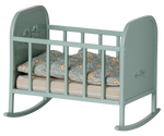 Blue Mint Cradle - My by Maileg: A small blue mint toy rocking cradle with side rails, delicate floral decorations, and patterned bedding inside, shown from a slight angle. It features gentle rocking legs and comes complete with a cozy sleeping bag—perfect for pretend play.