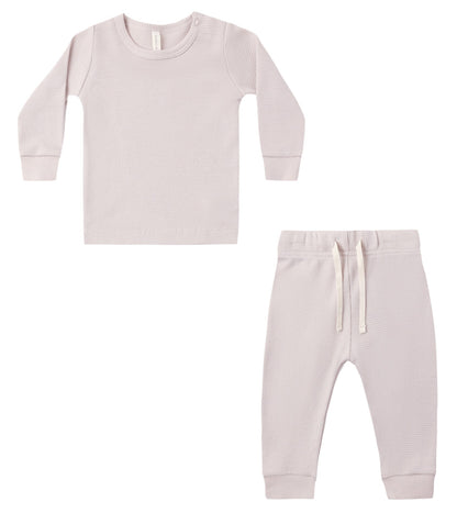 The Quincy Mae Baby Girls’ and Girls’ Waffle Top + Pant Set, featuring a light pink ribbed long-sleeve top with a snap at the shoulder and matching drawstring pants for a comfortable fit, is shown laid flat on a white background.