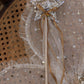 The Noralee Sun Crown + Wand features a gold sequin star wand with gold ribbons, shown on star-patterned tulle atop a woven cane chair—ideal for royal occasions or paired with the sun crown headband.