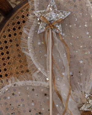 The Noralee Sun Crown + Wand features a gold sequin star wand with gold ribbons, shown on star-patterned tulle atop a woven cane chair—ideal for royal occasions or paired with the sun crown headband.