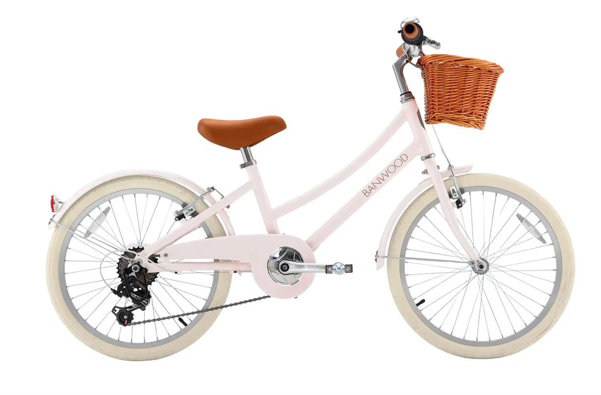 A light pink Banwood Kids’ Vintage Classic Bike featuring a brown leather seat, white tires, a wicker basket mounted on the front, and a small bell on the handlebars—perfectly embodying timeless Scandinavian design in a charming, child-friendly style.