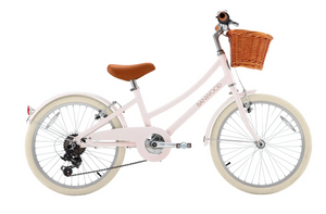 A light pink Banwood Kids’ Vintage Classic Bike featuring a brown leather seat, white tires, a wicker basket mounted on the front, and a small bell on the handlebars—perfectly embodying timeless Scandinavian design in a charming, child-friendly style.