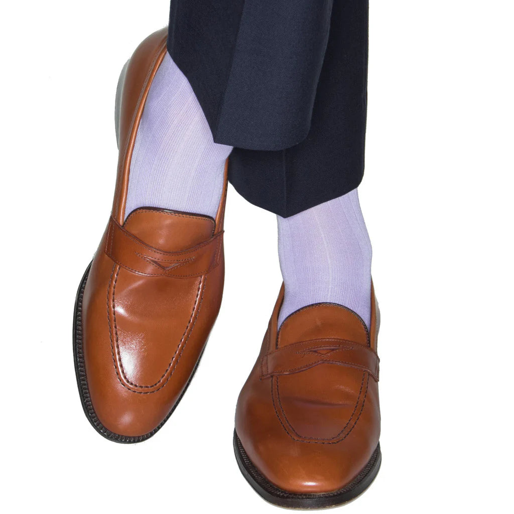 Person wearing Dapper Classics Lavender Solid Ribbed Cotton Sock Linked Toe Mid-Calf, brown leather loafers, and navy pants with feet crossed against a white background—a nod to timeless North Carolina style.