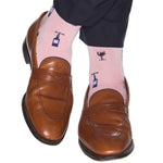 A person wearing tan loafers and the eye-catching Dapper Classics Merlot Mid Calf Socks in pink, adorned with a playful wine glass and bottle design, stands out effortlessly. Crafted with quality mercerized cotton, these stylish socks by Dapper Classics are a testament to fine American craftsmanship, proudly made in the USA.