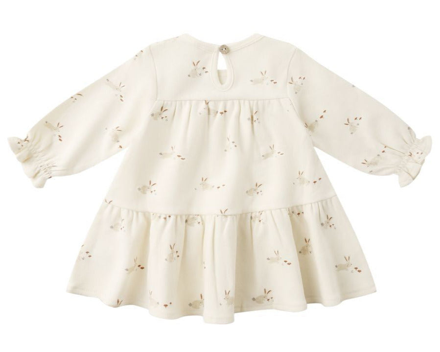 The Quincy Mae Baby Girls' and Girls' Tiered Jersey Dress is a cream-colored, long sleeve dress with a gathered skirt, subtle bunny face pattern, back button closure, and comes with matching bloomers.