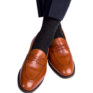 A person wearing dark dress pants, Dapper Classics Charcoal Solid Ribbed Fine Merino Wool Socks, made in North Carolina, and brown leather loafers with visible stitching.