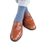 A person wearing light gray pants, brown leather penny loafers, and Dapper Classics Dress Navy and Sky Blue Herringbone Fine Merino Wool Mid-Calf Socks.