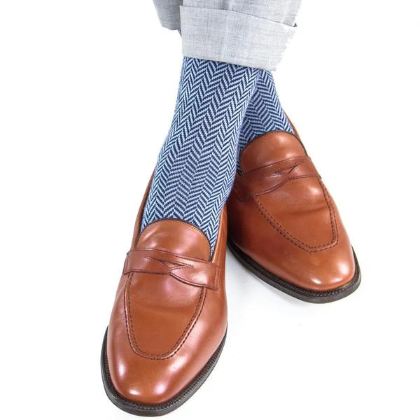 A person wearing light gray pants, brown leather penny loafers, and Dapper Classics Dress Navy and Sky Blue Herringbone Fine Merino Wool Mid-Calf Socks.