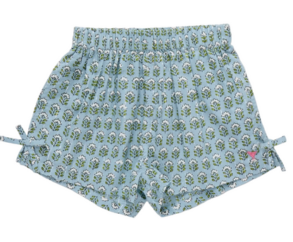 The Girls’ Jules Short by Pink Chicken showcases a Blue Prairie Blockprint adorned with a charming green and white leaf pattern, featuring an elastic waist for extra comfort, adorable side bows, and a small pink butterfly logo near the bottom hem.