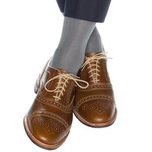 Someone wearing Dapper Classics Steel Gray Solid Ribbed Cotton Sock Linked Toe Mid-Calf and brown brogued leather dress shoes sits with their legs crossed.