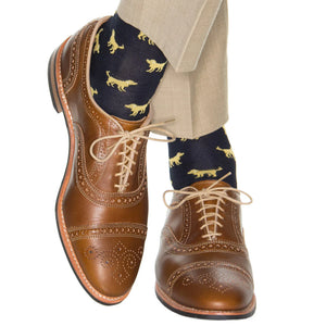 A person wearing light brown brogue dress shoes, beige pants, and Dapper Classics Navy with Yolk Dog Cotton Sock Linked Toe Mid-Calf.