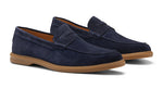 The Peter Millar Excursionist Penny Loafer is a pair of navy blue water-resistant suede loafers with brown rubber soles, displayed side by side on a white background.