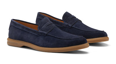 The Peter Millar Excursionist Penny Loafer is a pair of navy blue water-resistant suede loafers with brown rubber soles, displayed side by side on a white background.