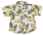 The Boys’ Jack Shirt from Pink Chicken features short sleeves and a fun pattern of yellow bananas and green leaves on a crisp white background, complete with natural wood buttons for a stylish touch. This warm-weather classic also offers a convenient chest pocket.