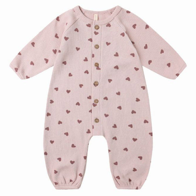 The Quincy Mae Baby Girls' Waffle Long Sleeve Jumpsuit features a light pink knit with brown heart print, front coconut buttons, and is shown on a plain white background.