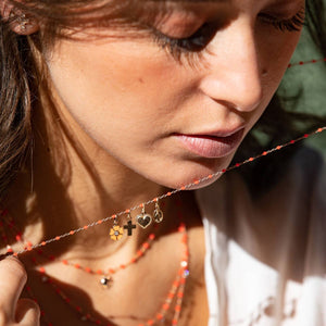 Close-up of a woman with a thoughtful expression, her face partially obscured by a Gigi Clozeau Cross Pendant in 18 carat yellow gold beaded necklace.