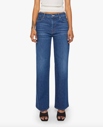 A person wears Mother’s Lil Kick It high-waisted, wide-leg blue jeans—crafted for petites with front and back pockets—paired with a white sleeveless top and black open-toe heels, standing against a white background.