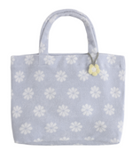 The Terry Beach Bag by Rylee & Cru comes in light blue and showcases white flower patterns with a small yellow flower charm, making it an ideal beach accessory.