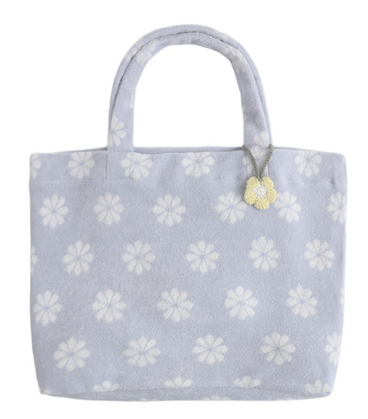 The Terry Beach Bag by Rylee & Cru comes in light blue and showcases white flower patterns with a small yellow flower charm, making it an ideal beach accessory.