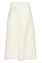 The A-Line Skirt by TWP is a white linen midi skirt with an A-line silhouette, featuring subtle beige floral embroidery.