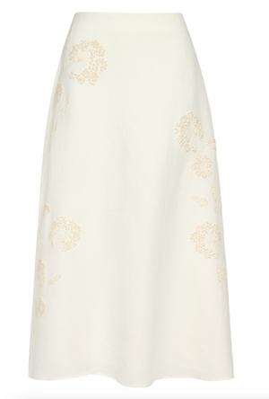 The A-Line Skirt by TWP is a white linen midi skirt with an A-line silhouette, featuring subtle beige floral embroidery.