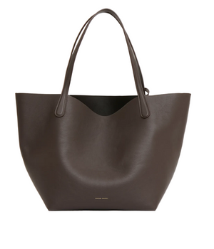 The Everyday Soft Tote by Mansur Gavriel is a large brown tote bag crafted from Italian calf leather, featuring two shoulder straps and subtle branding near the base. Photographed against a plain white background, this spacious leather tote blends understated elegance with versatile functionality for daily use.