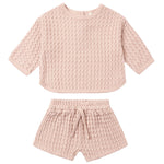 The Quincy Mae Baby Girls’ and Girls’ Flynn Set features a light pink, short-sleeve top and matching shorts in a cozy waffle knit, complete with a drawstring waistband—perfect for comfortable everyday wear.
