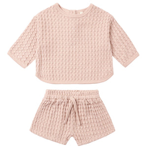 The Quincy Mae Baby Girls’ and Girls’ Flynn Set features a light pink, short-sleeve top and matching shorts in a cozy waffle knit, complete with a drawstring waistband—perfect for comfortable everyday wear.