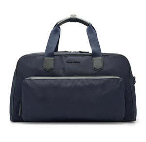The Peter Millar Pursuit Duffle is a navy blue bag with black handles, a front zippered pocket, and a main compartment, ideal for travel. Shown against a white background.