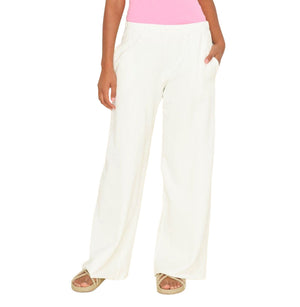 Model wears the Xirena Emmette Sweatpant, a loose-fitting wide leg sweatpant in white organic mineral wash terry, paired with a pink top and sandals, hands in pockets against a white background.
