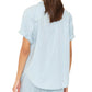 A person is seen from the back wearing the Xirena Channing Chambray Shirt in light blue cotton, styled with rolled cuffs and matching pants—a versatile essential for any wardrobe.
