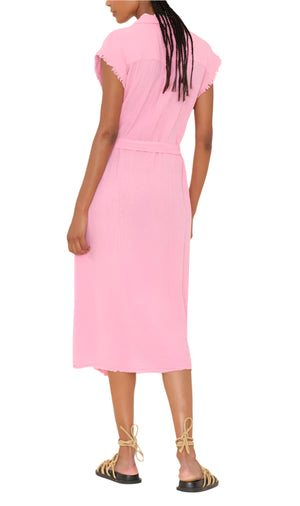 A person is shown from the back against a white background wearing the Xirena Aliza Dress, a belted, short-sleeve pink button-front midi dress, paired with black sandals featuring beige laces.