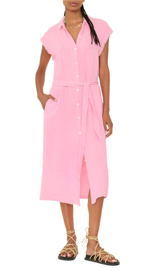 A person wears the Xirena Aliza Dress—a light pink, button-front midi in double-faced cotton gauze with adjustable tie-belt and side pockets—paired with strappy flat sandals.