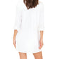 A woman is shown from the back wearing the Xirena Tyson Dress, a white, button-front mini shirtdress with long sleeves rolled up.