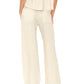 Model shown from the back wearing Xirena's Romany Pant in a loose, cream hue with an elastic waist, paired with a matching short-sleeve top and beige sandals, set against a plain background.