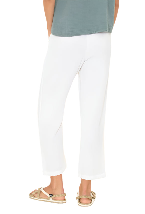Model wearing the Ozzie Pant by Xirena—white cotton gauze wide-leg pants with an elasticized drawstring waist—paired with a loose greenish-grey top and beige rope sandals, shown from the back against a plain white background.