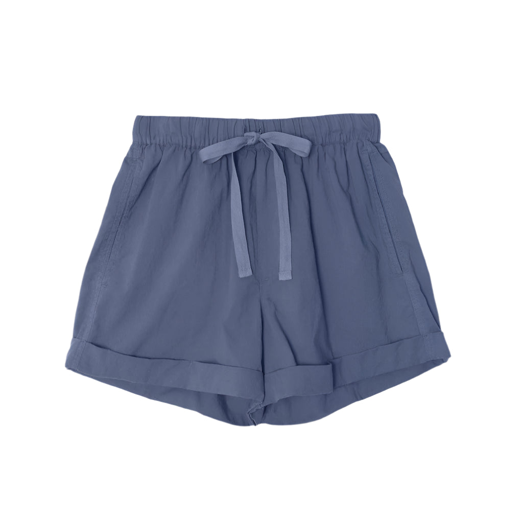 The Declan Short by Xirena is a light blue, lightweight woven cotton short with an elastic drawstring waist, side seam pockets, and folded hems, shown laid flat on a white background.